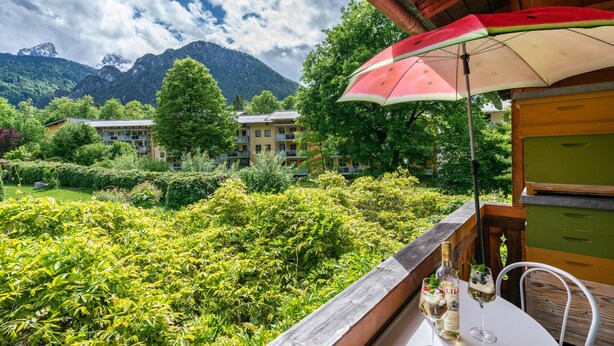 Een balkon met uitzicht op weelderige begroeiing en bergen, een tafel met drankjes, en een rood-witte parasol.