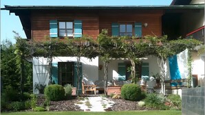 Een huis met twee verdiepingen, een overdekt terras, een kleine tuin en een houten bank.