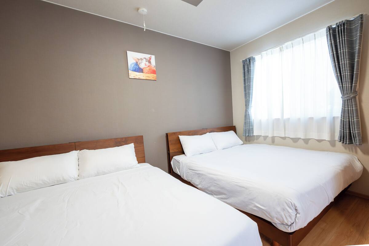A hotel room with two single beds, a wooden headboard, a ceiling light, a window with curtains, and a picture on the wall.