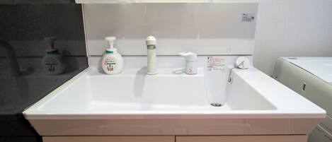 Een wit badkamermeubel met twee lades, een spiegel erboven en drie handdesinfecterende flesjes op het aanrecht.