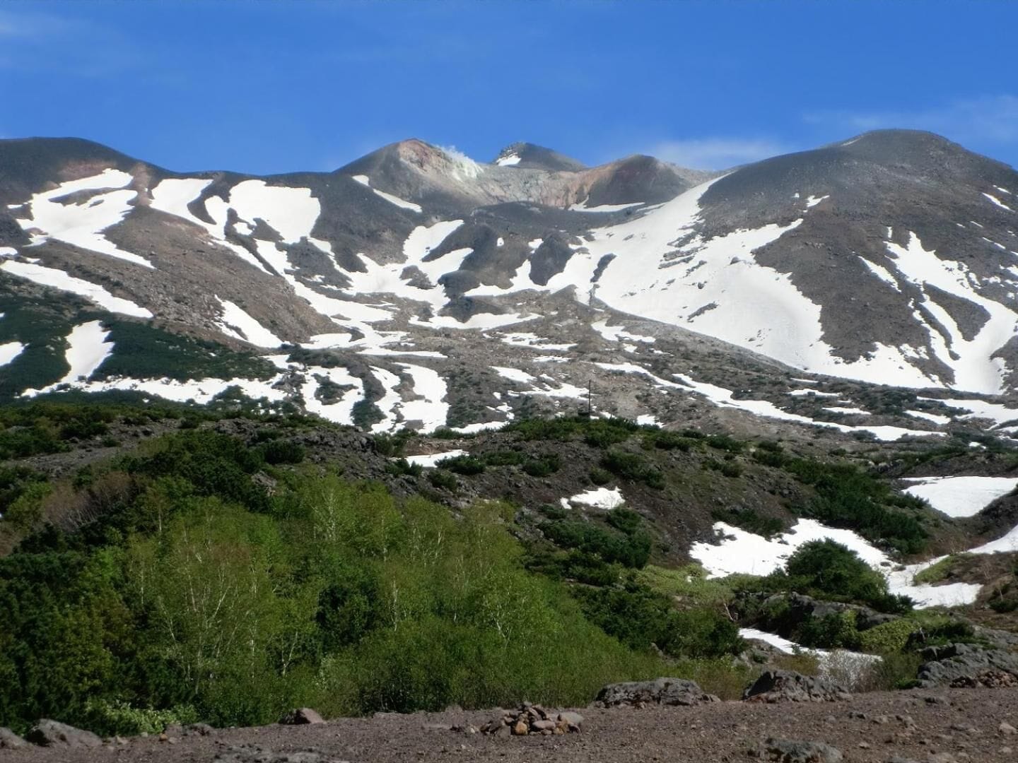 A mountainous landscape with snow patches and green vegetation.