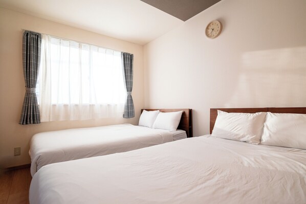 A hotel room with two beds, a window with curtains, a clock on the wall, and a wooden headboard. - Stay in Biei (Biei)
