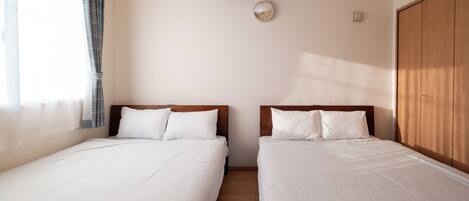 A hotel room with two beds, a wooden wardrobe, a ceiling light, and a wall clock.