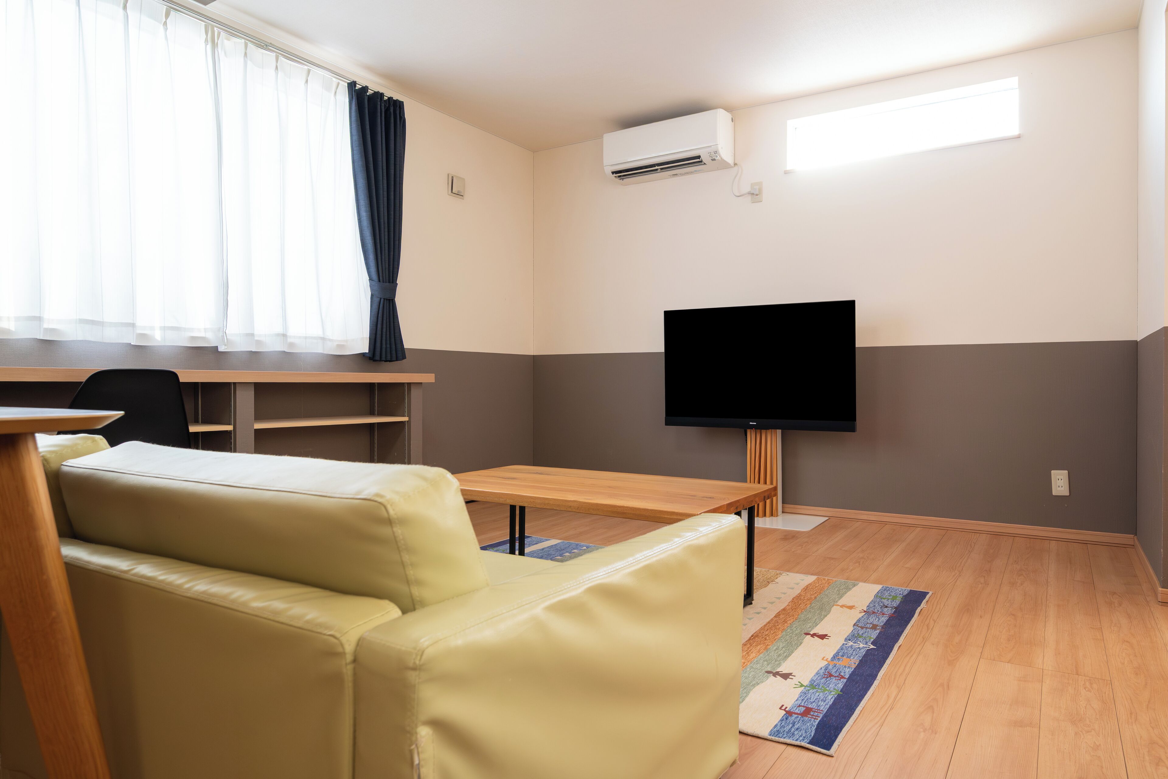 Una sala de estar moderna con un sofá, una mesa de madera, un televisor de pantalla plana y una ventana con cortinas.