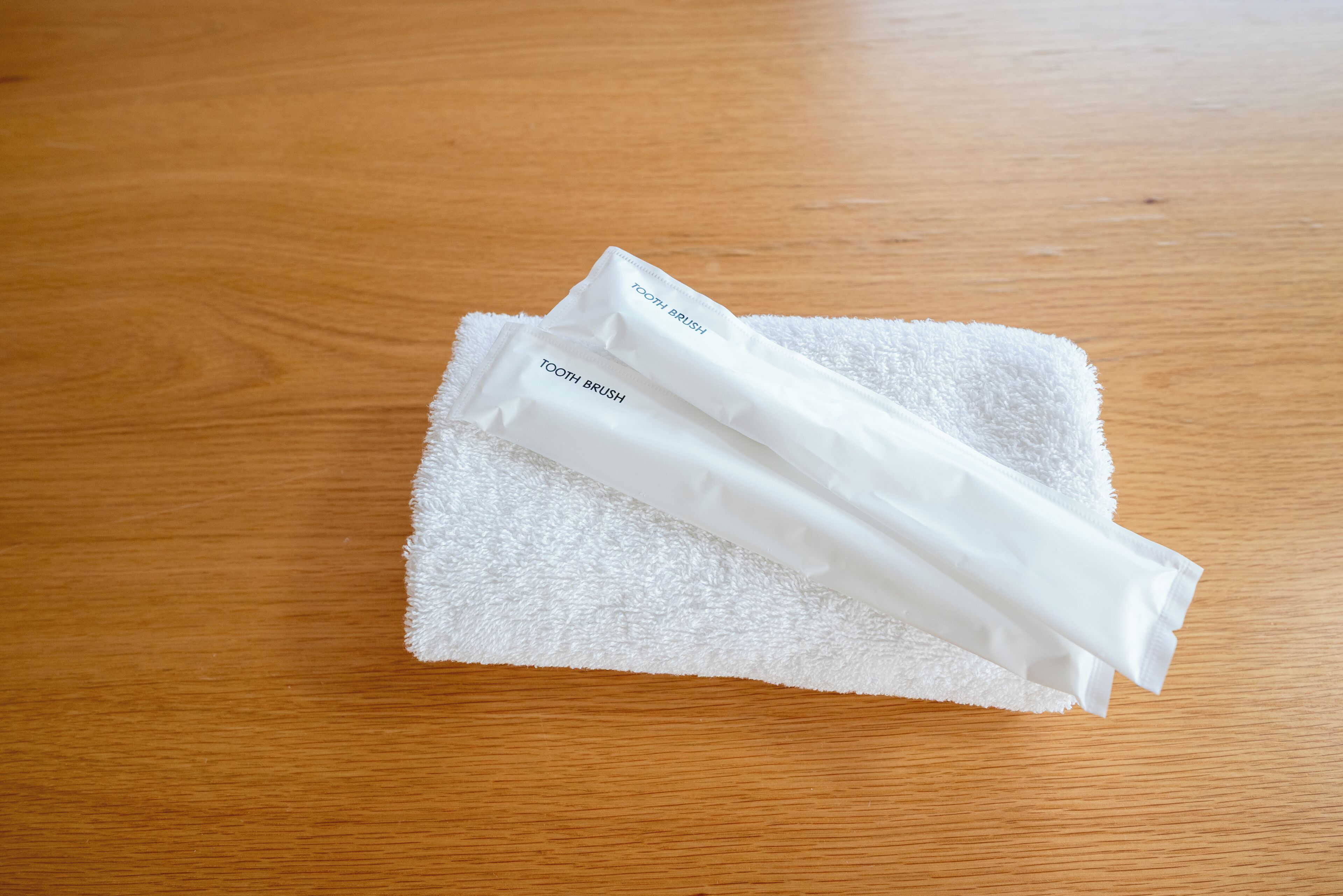 Two white toothbrushes on a white towel on a wooden surface.