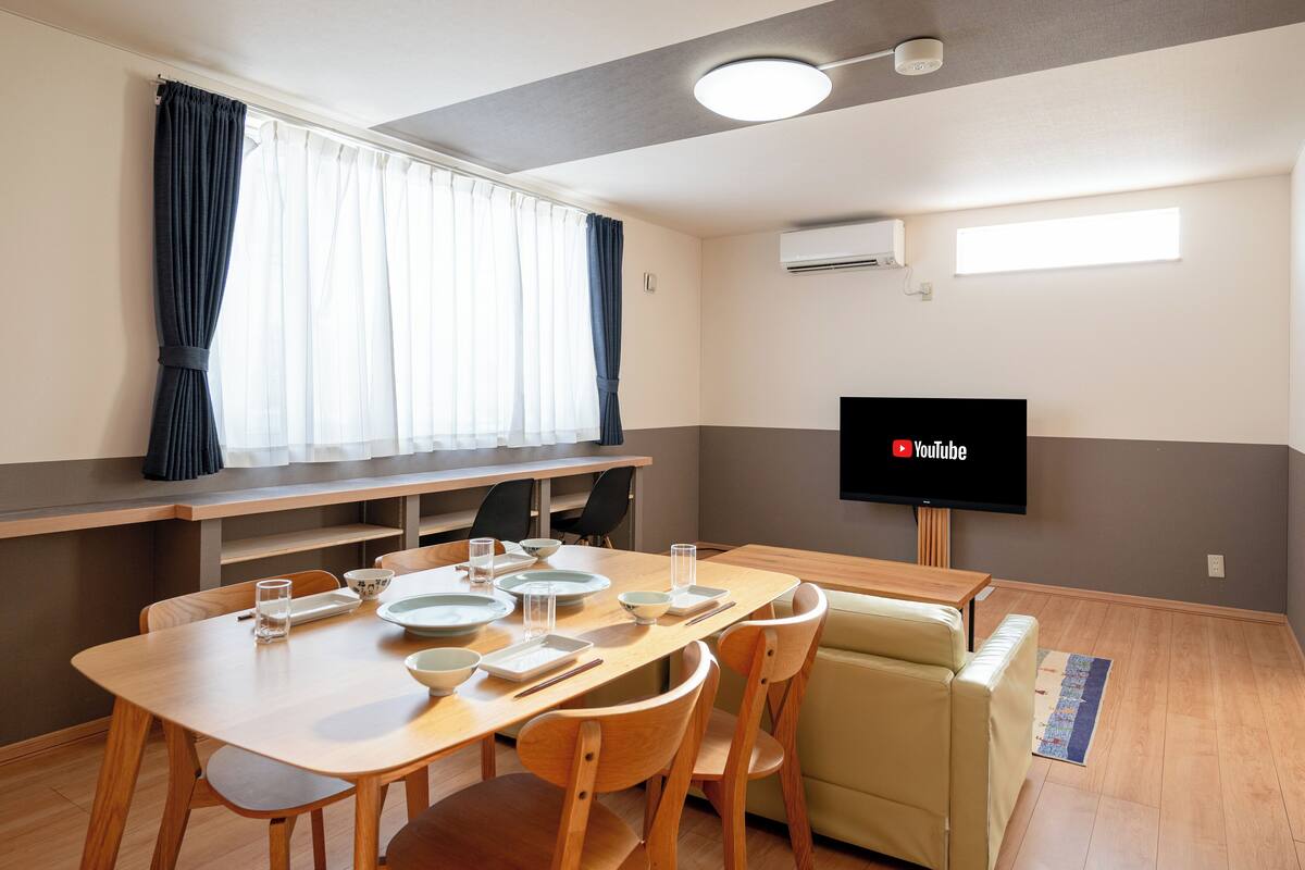 A dining area with a table set for four, a sofa, and a flat-screen TV mounted on the wall.
