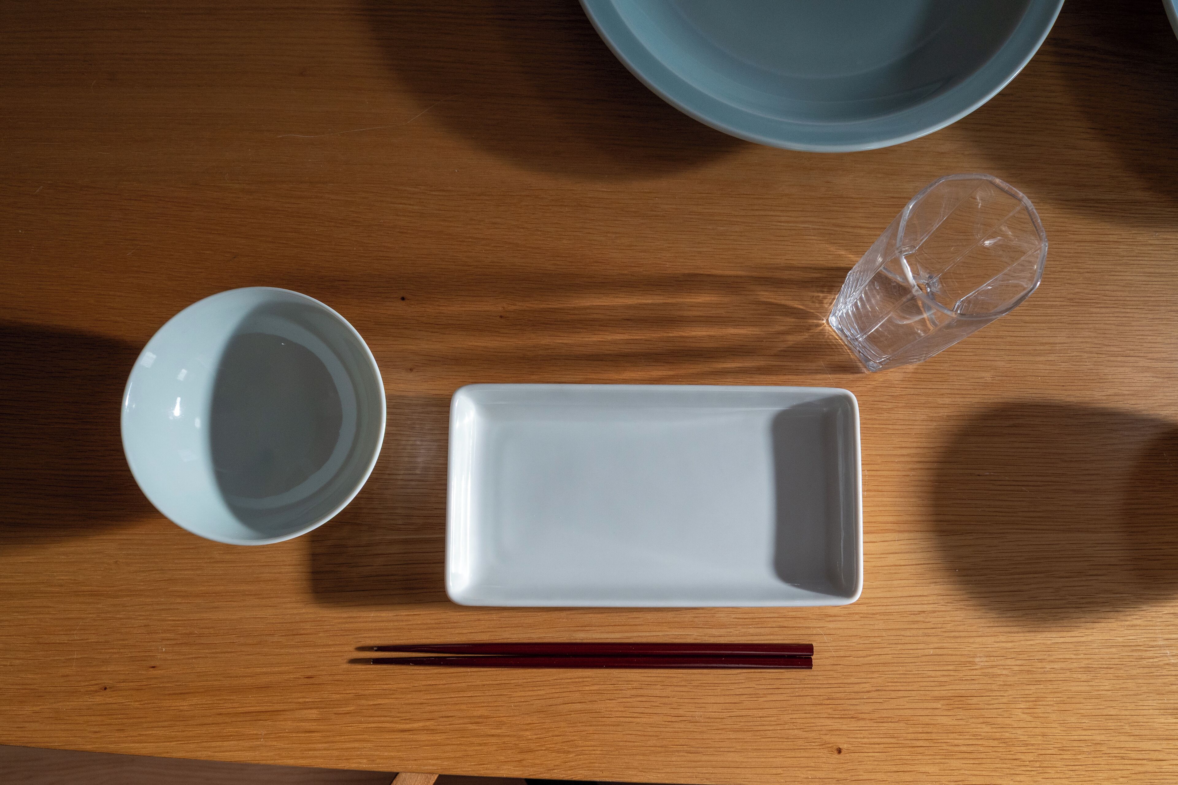 A wooden table with a white rectangular plate, a white bowl, and a clear glass.