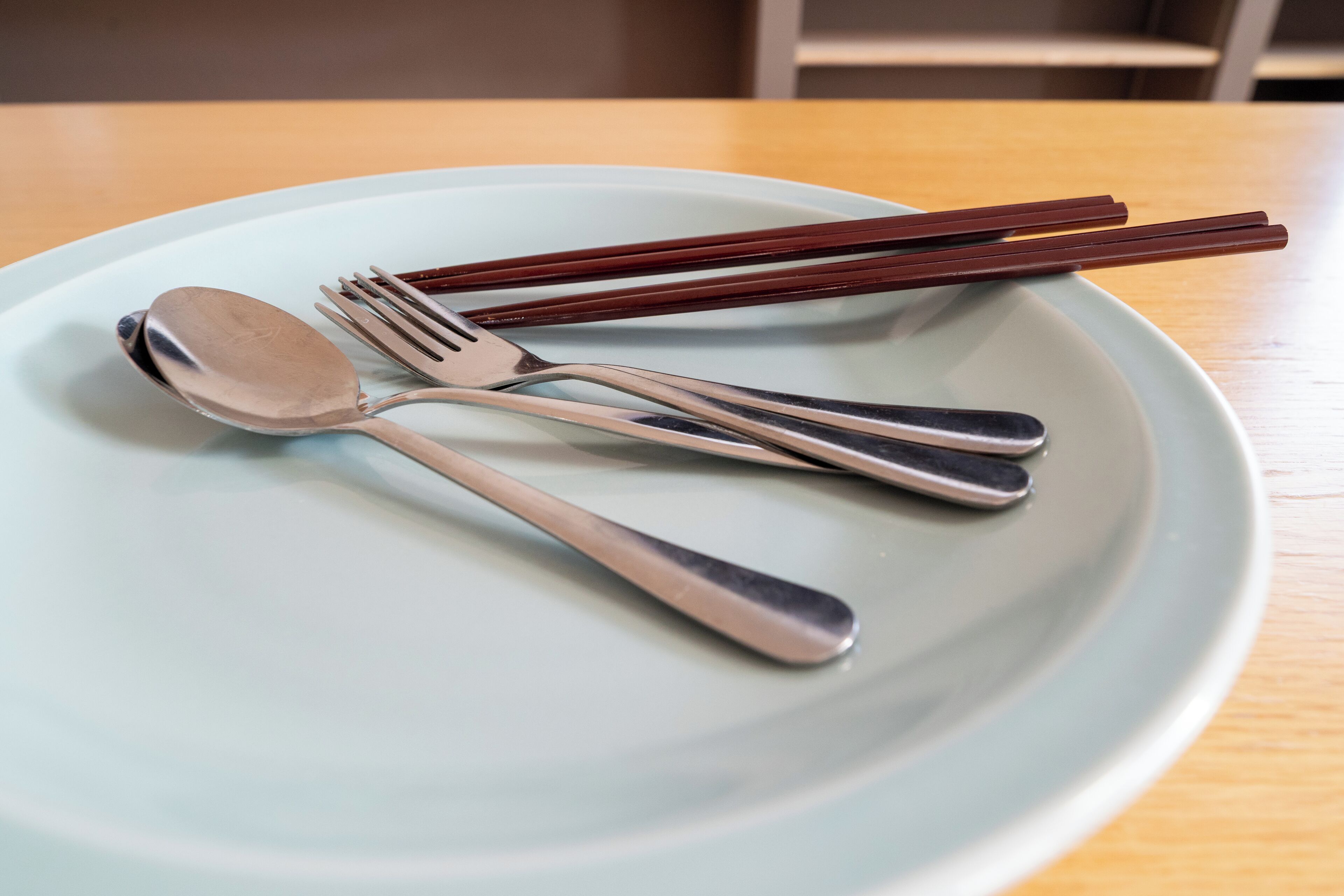 A plate with a spoon, fork, and chopsticks on a table.