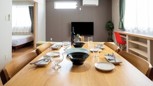 Een eetgedeelte met een houten tafel voor vier personen, een aan de muur bevestigde flatscreen-tv en een raam met gordijnen.