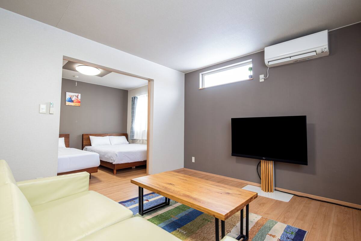 A modern hotel room with a wooden table, two beds, a TV, and an air conditioning unit.