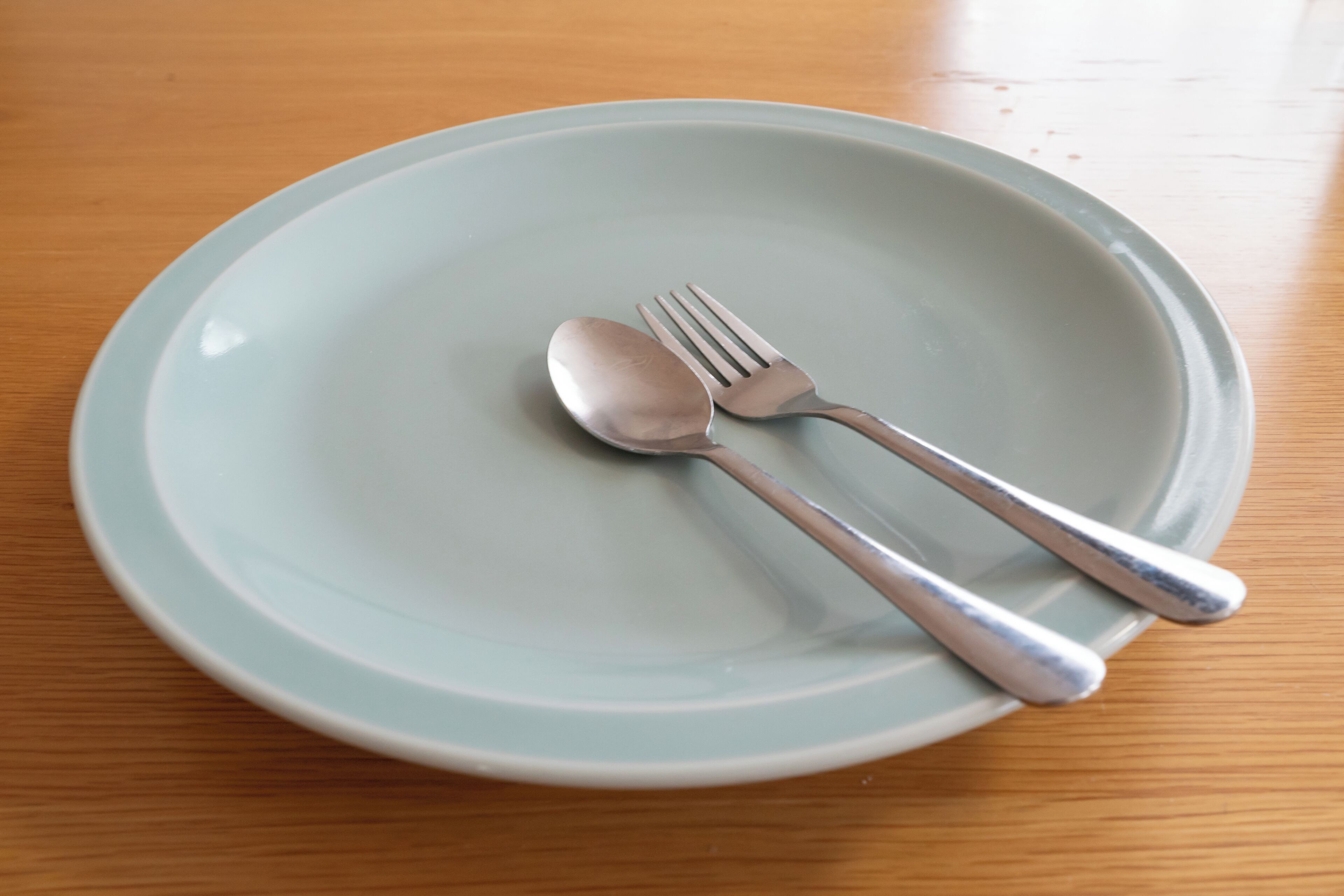 A round, light blue plate with a spoon and fork on a wooden table.
