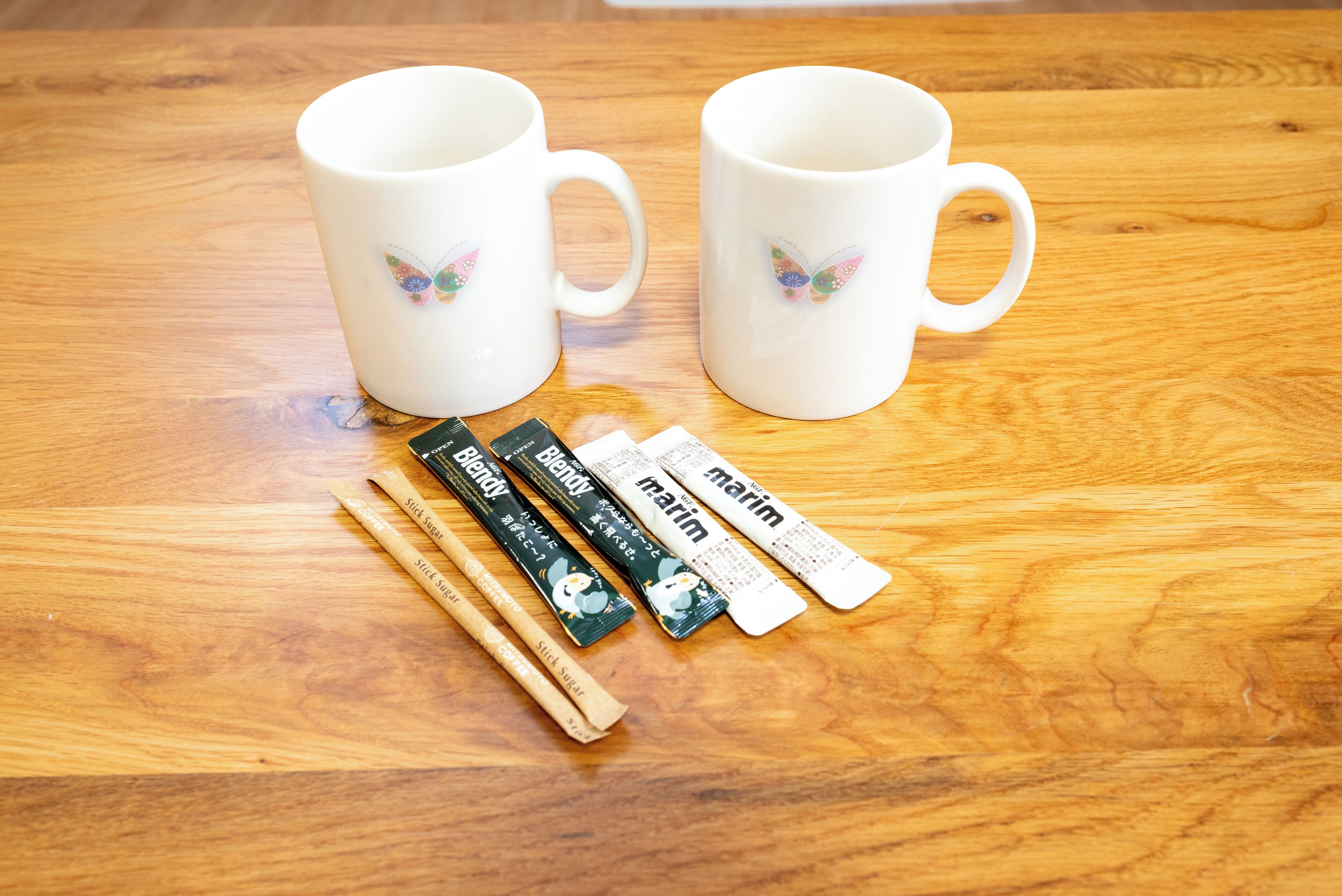 Two white ceramic mugs with butterfly designs on a wooden table.