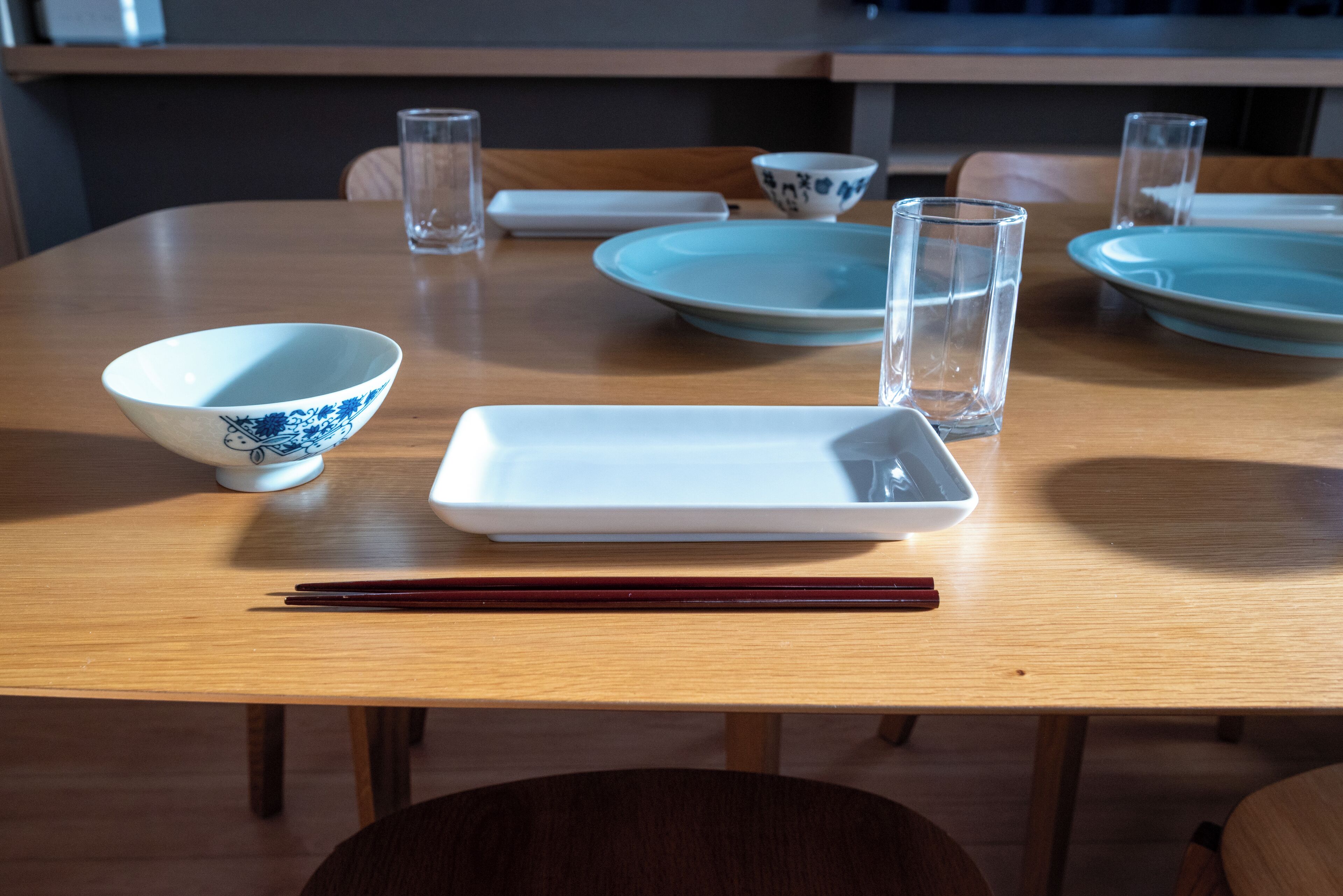 A dining table with a white rectangular plate, a blue and white bowl, and two clear glasses.