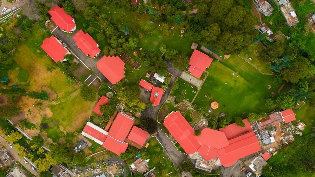 An aerial view of a residential area with multiple houses, each featuring red roofs, surrounded by green lawns and trees.