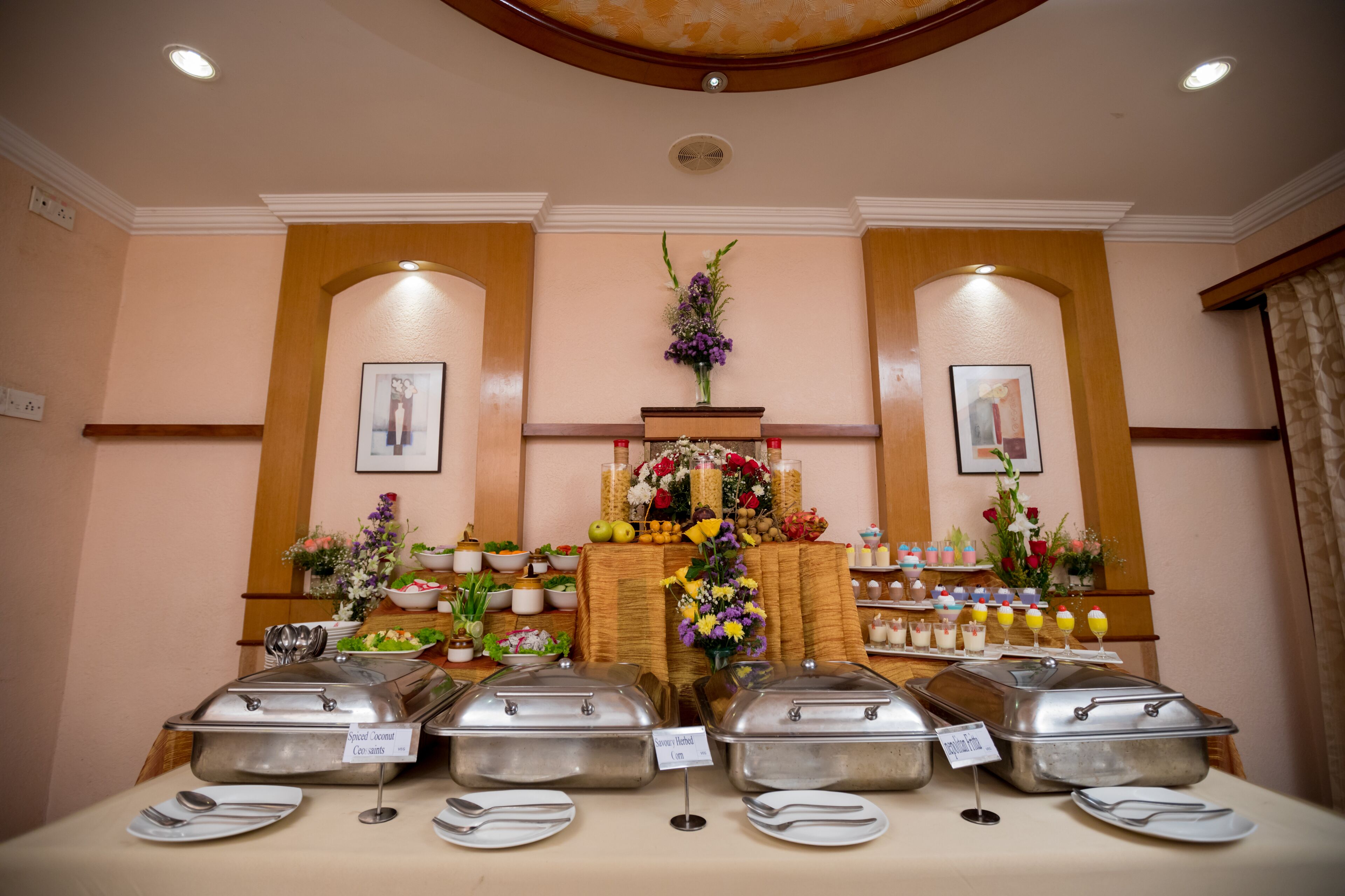 Montaje de bufé con múltiples estaciones de servicio de alimentos, un centro de mesa floral y obras de arte enmarcadas en las paredes.