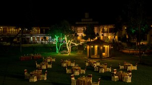 An outdoor event space with round tables and chairs, a gazebo, and a well-lit lawn area. - Hotel Kodai International (Kodaikanal)