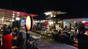 An outdoor dining area with tables and chairs, a covered seating area, and a food service counter. - Golite Hostel-Albay (Legazpi)