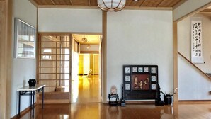 Um quarto espaçoso com piso de madeira, uma porta tradicional japonesa deslizante, um painel decorativo preto e dourado e um pendente.