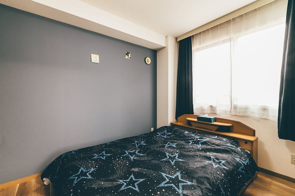 A bedroom with a bed, a nightstand, a window with curtains, and a wall clock.