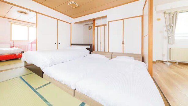 A hotel room with two beds, a wooden ceiling, a radiator, and a window with curtains. - Stay in Otaru (Otaru)