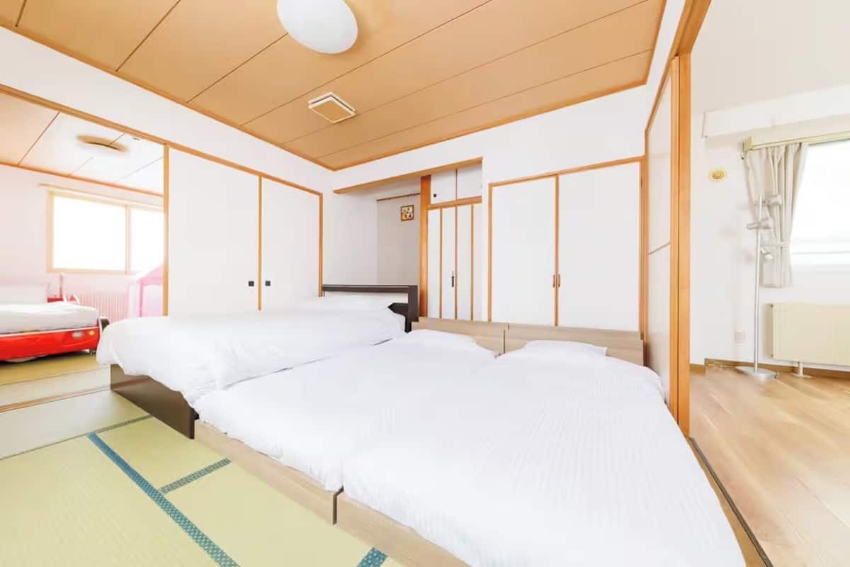 A hotel room with two beds, a wooden ceiling, a radiator, and a window with curtains.