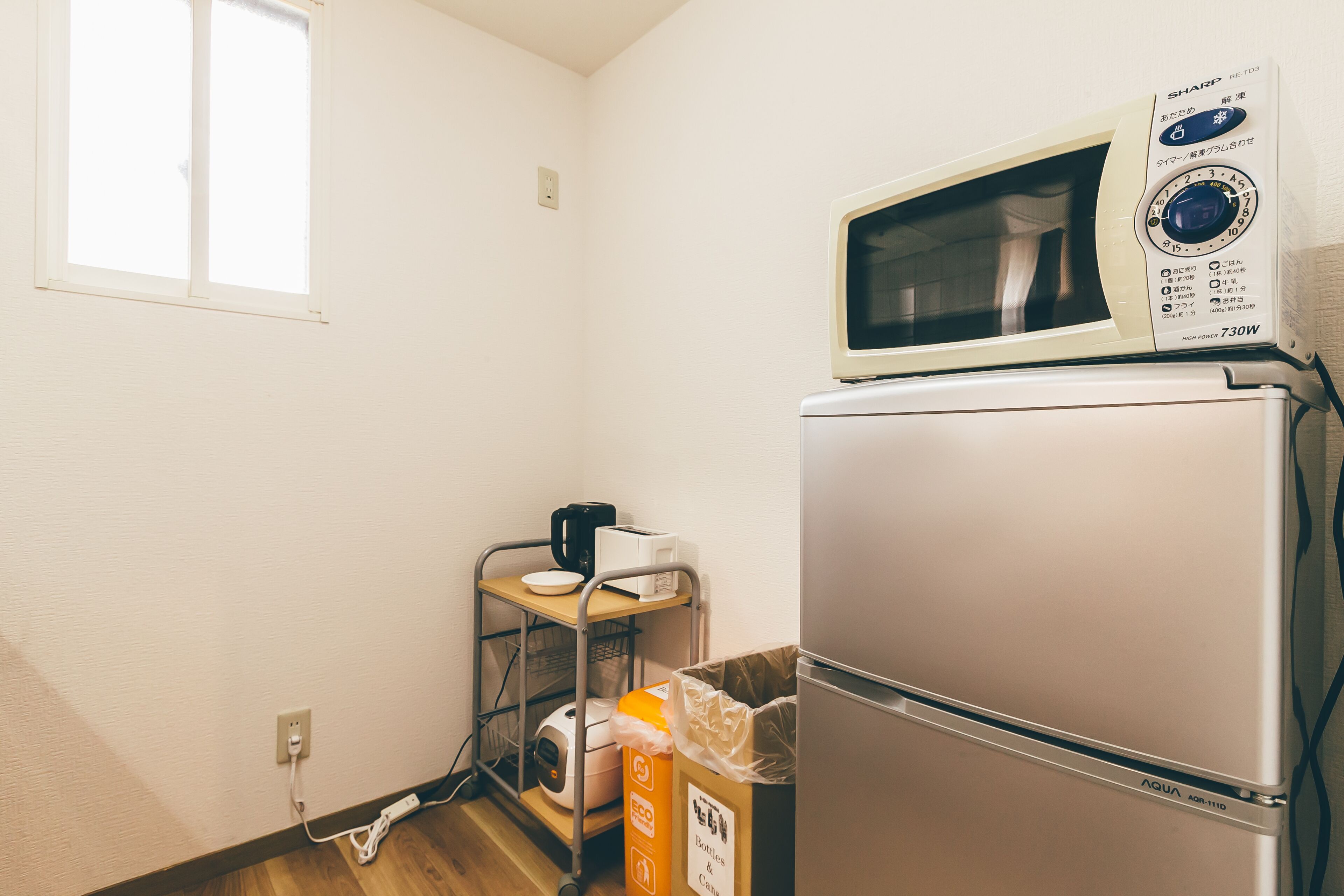 A compact kitchen with a microwave and refrigerator, a small window, and a utility cart with a coffee maker.