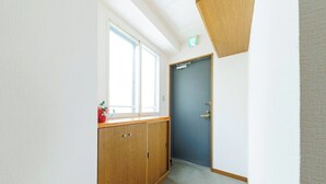 A narrow hallway with a wooden cabinet, a blue door, and a window with natural light. - Stay in Otaru (Otaru)