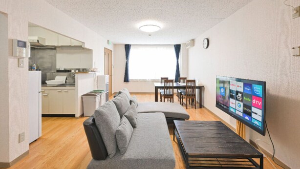 A compact living space with a kitchenette, sofa, dining table, and a flat-screen TV.