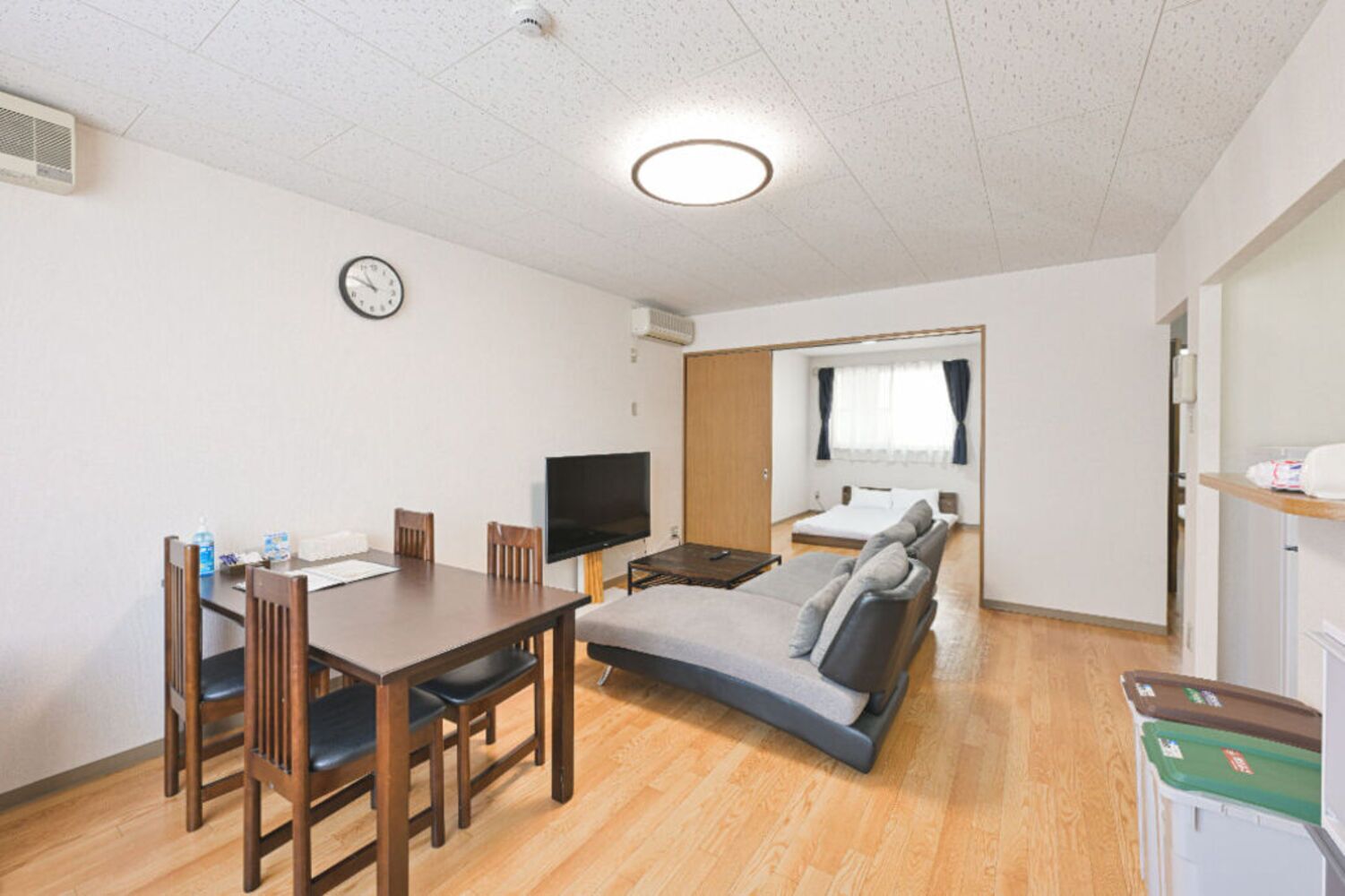 A compact room with a dining table, chairs, a flat-screen TV, a sofa, and a bed.