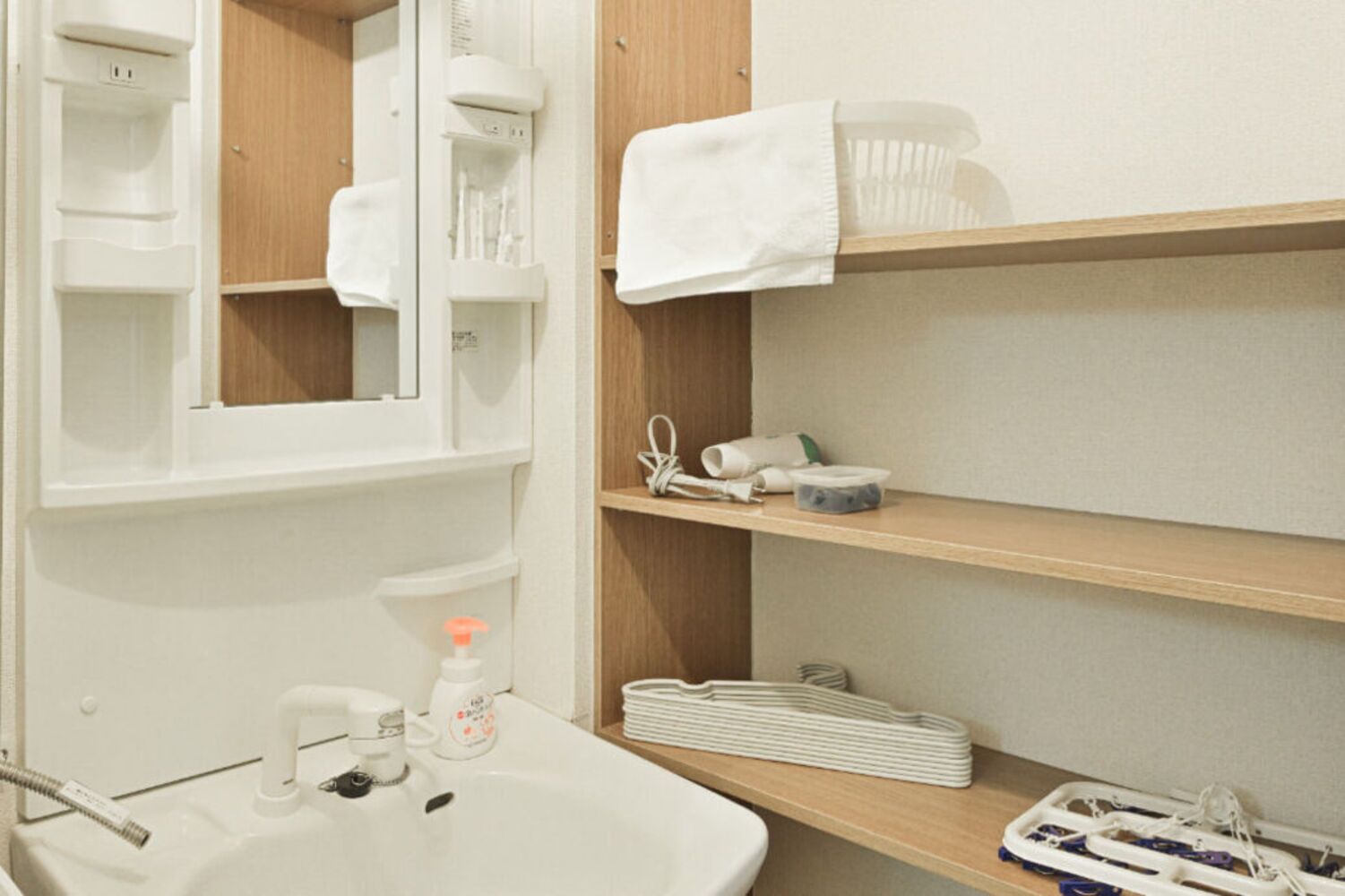 A bathroom with a sink, mirror, shelves with toiletries, and a towel rack.