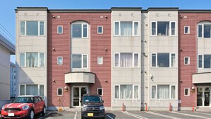 A multi-story building with a red facade, multiple windows, and a parking lot with cars.