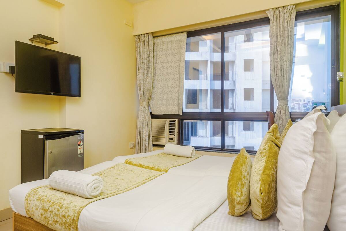 A hotel room with a bed, a television, a small refrigerator, and a window with curtains.