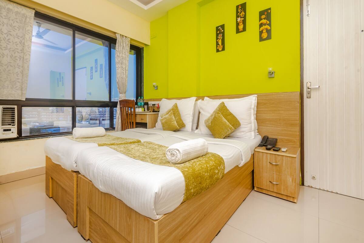 A hotel room with a large bed, a wooden nightstand, a desk with a chair, and a bright green wall.