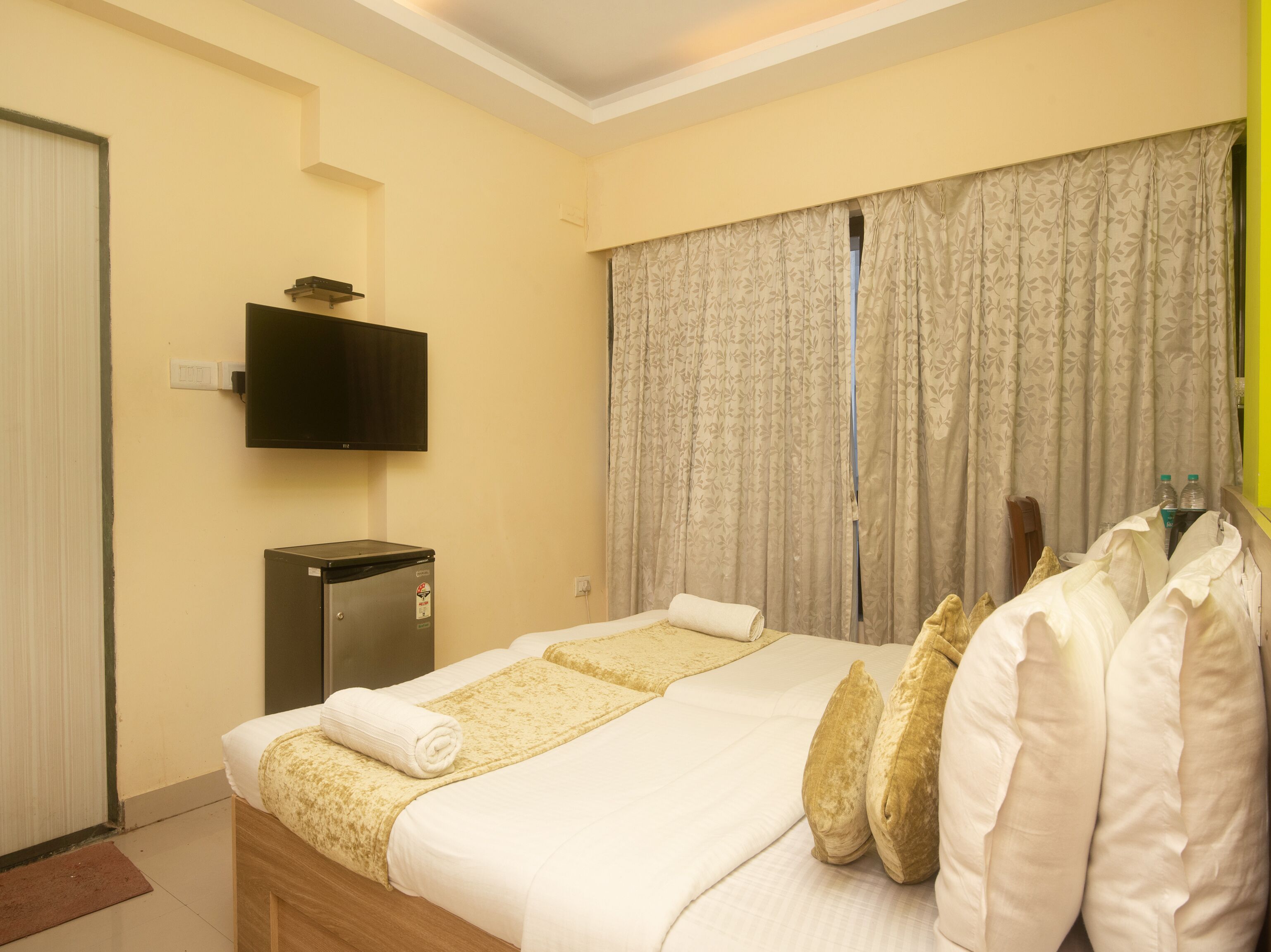 Una habitación de hotel con una cama, televisión, minibar y cortina.