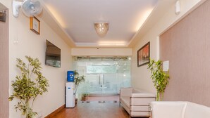 A reception area with a wooden floor, a white sofa, a water dispenser, and a potted plant. - Tuliip Residency (Mumbai)