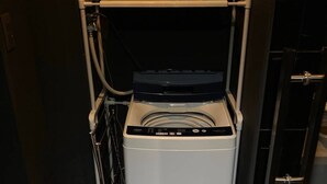 A compact, front-loading washing machine in a small laundry room with a shelf above it. - Bettei Shinimamiya (Osaka)