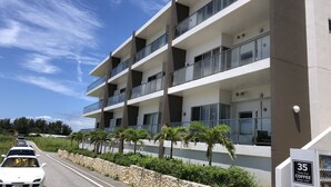 Un immeuble à plusieurs étages doté de balcons, d’un mur de soutènement en pierre et d’une enseigne indiquant un café.
