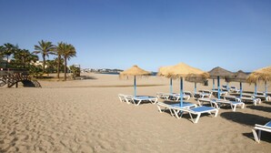A beach with sun loungers and thatched umbrellas.