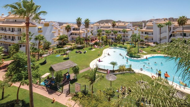 A resort with a large pool, palm trees, and multiple buildings with balconies.