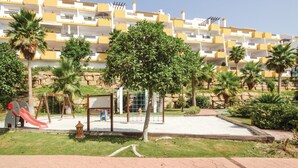 A playground with a slide and swings, surrounded by a landscaped garden with palm trees and a stone wall.