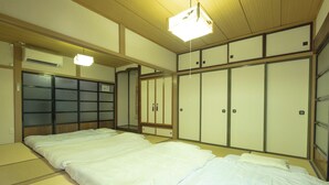 Ein traditioneller japanischer Raum mit Tatami-Boden, niedrigem Bett, Schiebetüren und Deckenventilator.