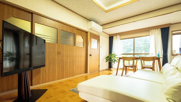 Ein modernes Wohnzimmer mit Flachbildfernseher, einem weißen Sofa, Holzboden und einem großen Fenster mit Vorhängen.