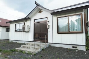 Simple, single-story building with a white facade, dark brown door and window frames, and a metal roof.