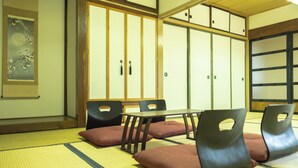 Ein traditioneller japanischer Raum mit Tatami-Boden, einem niedrigen Tisch und schwarzen Stühlen mit Ausschnitten im Rücken.
