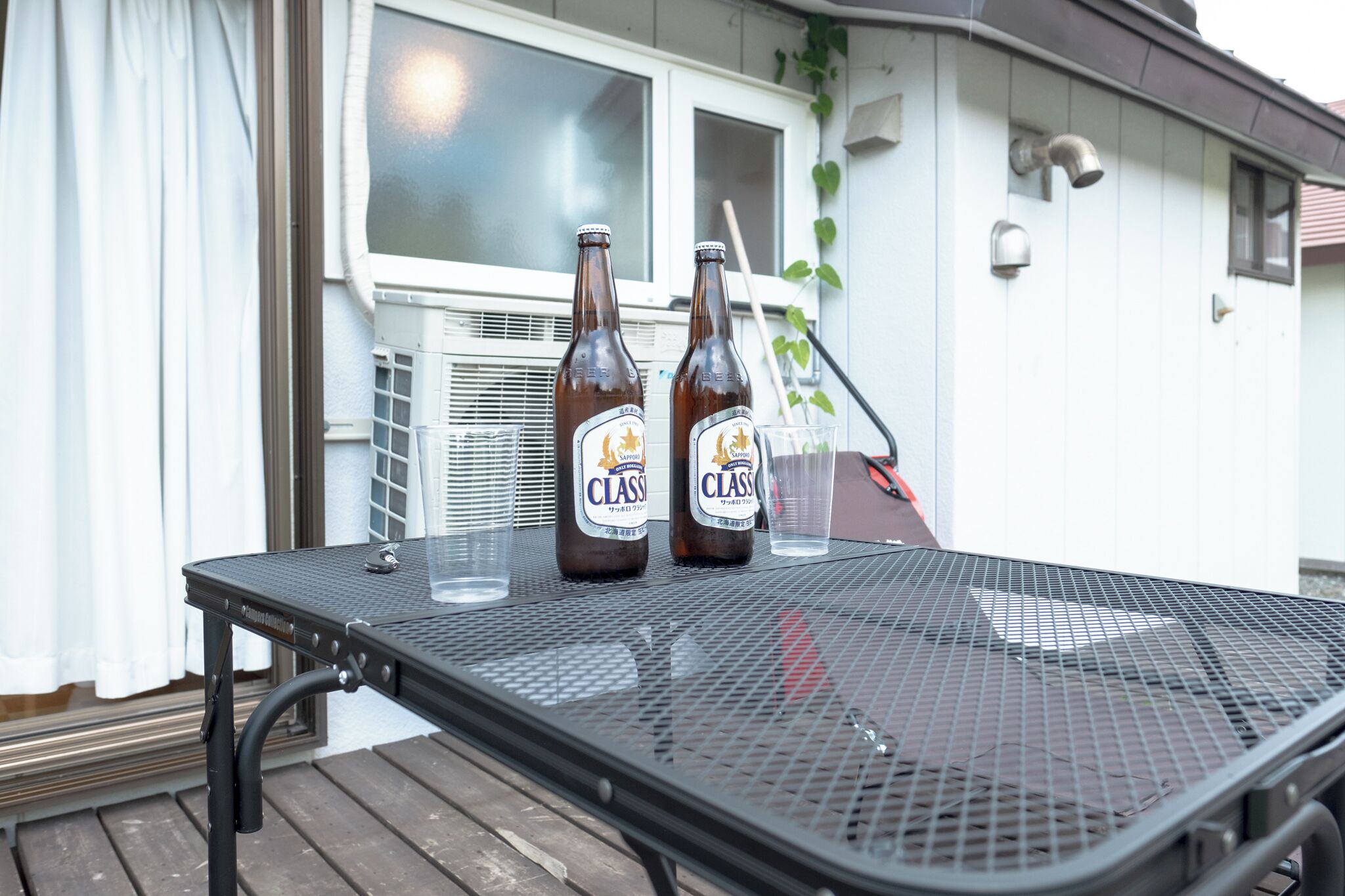 Una mesa metálica con dos botellas de cerveza y un vaso sobre una cubierta de madera.