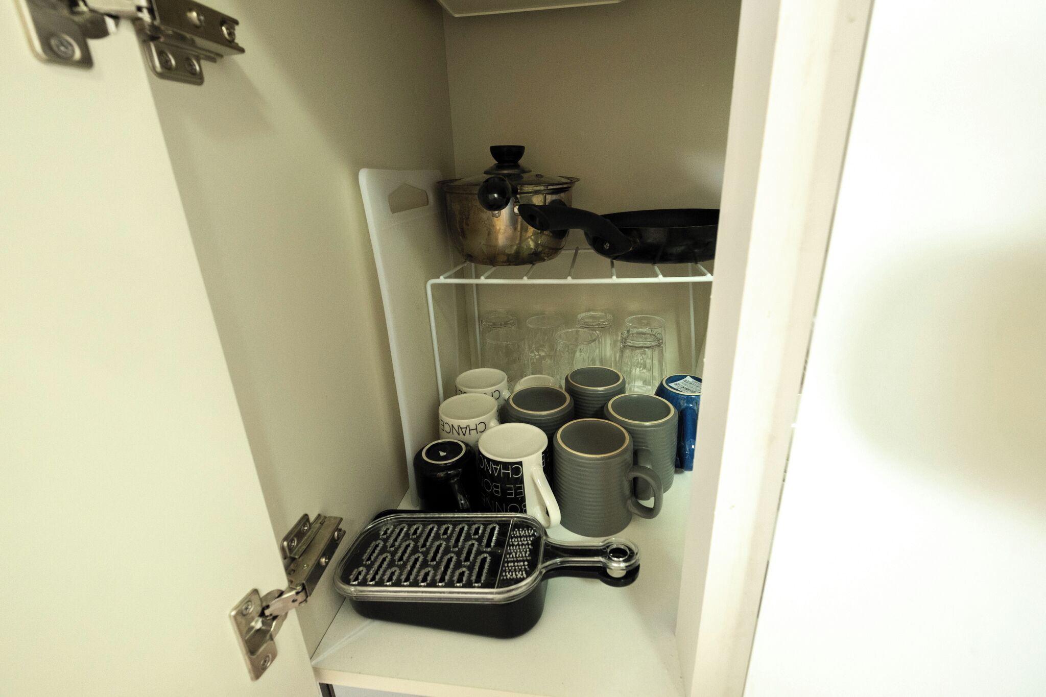 Une cuisine avec un meuble blanc contenant une poêle, une casserole et plusieurs tasses.