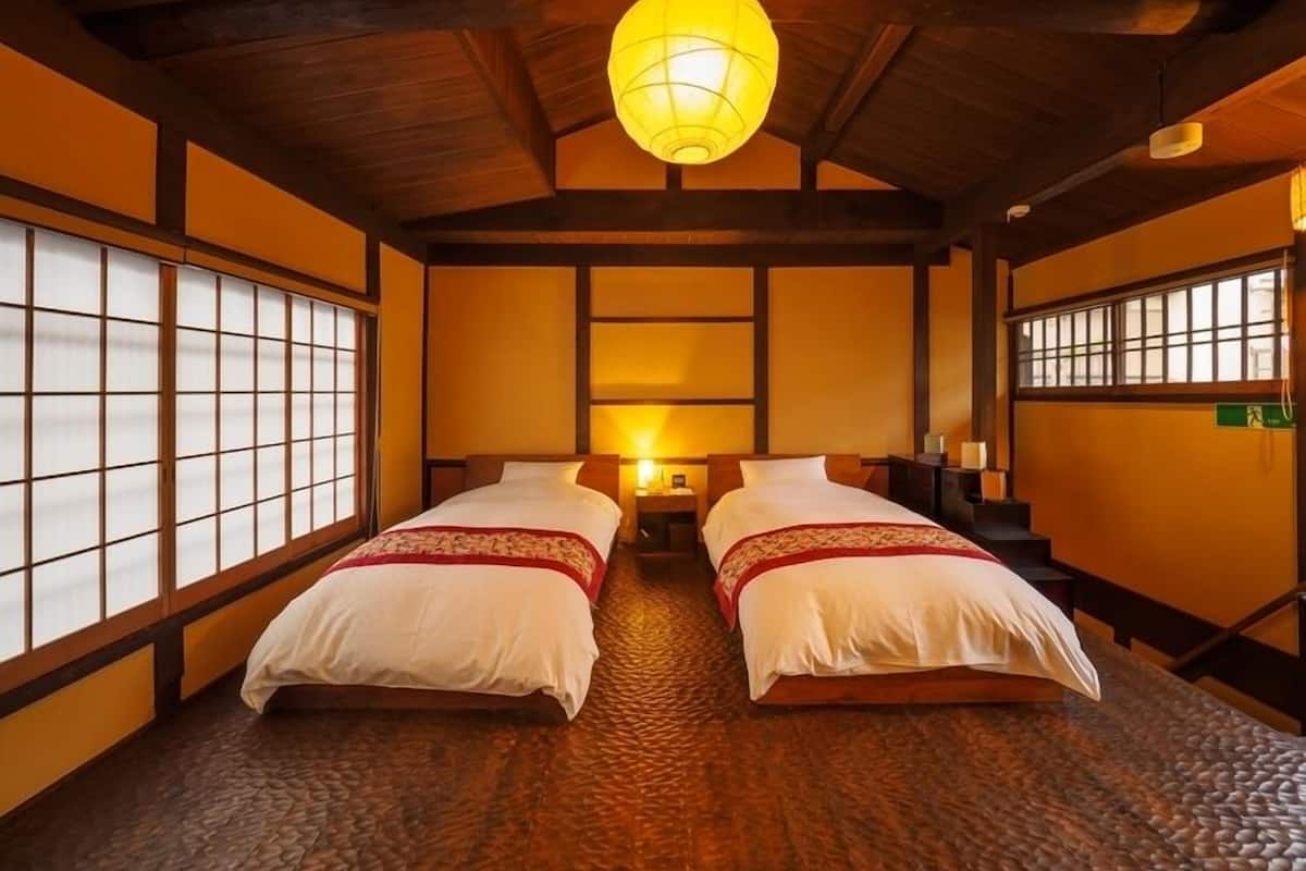 Una habitación tradicional japonesa con suelo de tatami, dos camas con ropa blanca, un farol de papel colgante y puertas shoji.