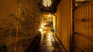 A narrow alleyway with bamboo plants on one side and a wooden gate on the other.