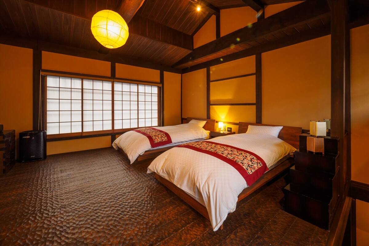 A traditional Japanese-style room with tatami flooring, two beds with red bedding, a shoji screen window, and a wooden ceiling.