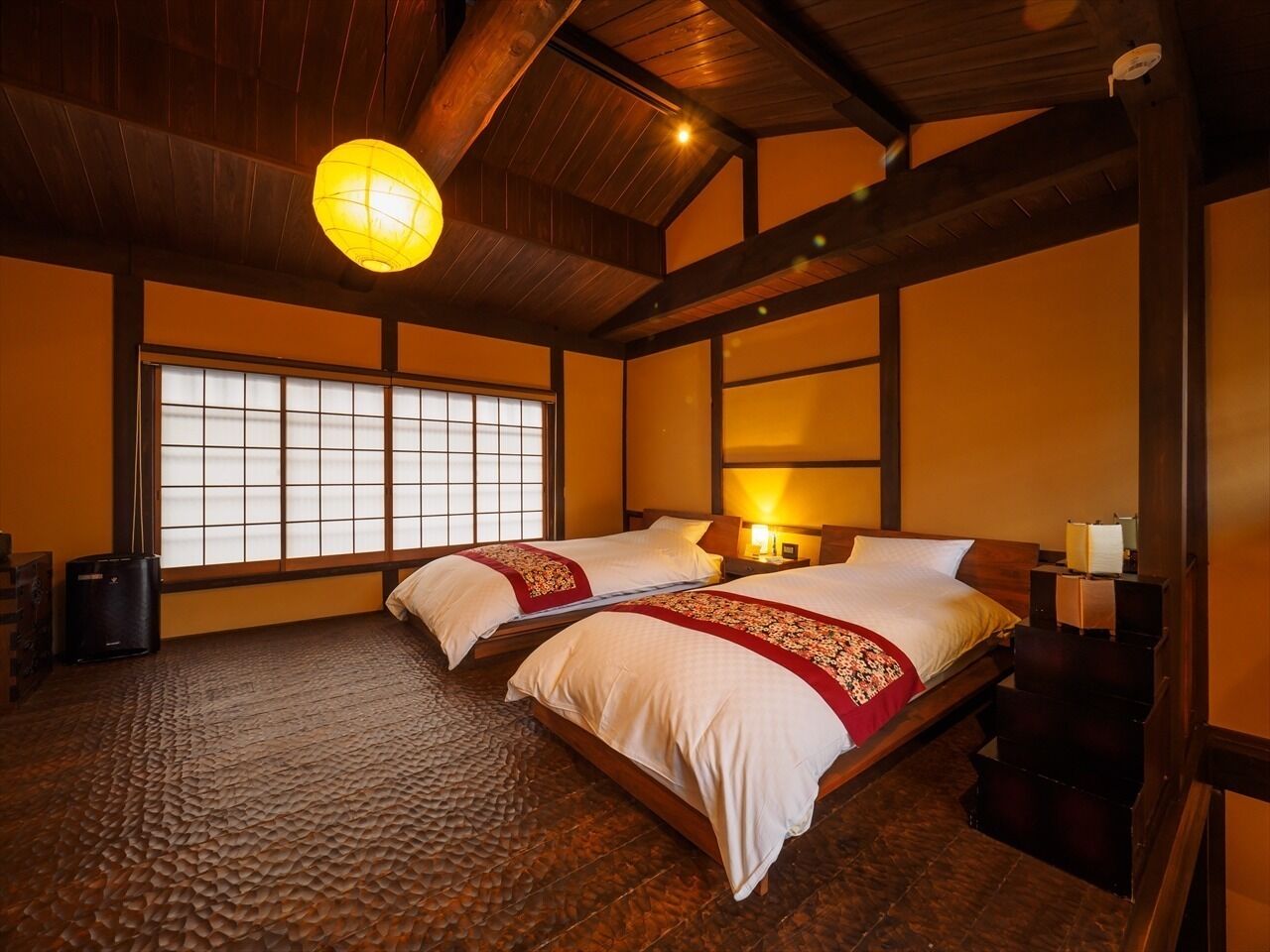 A traditional Japanese-style room with two beds, wooden beams, tatami flooring, and a large window.